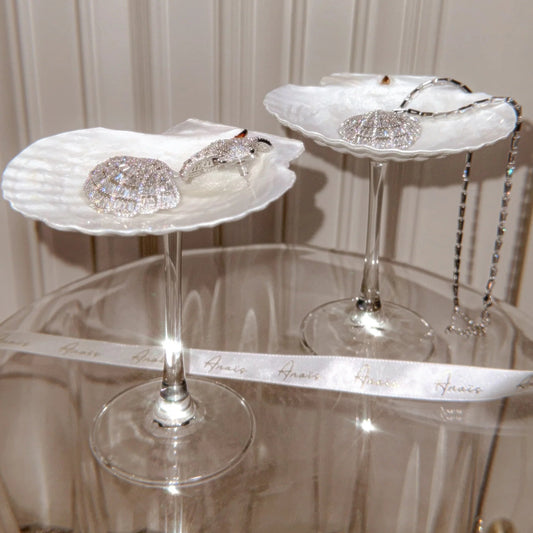 Two decorative shell-shaped stands on a reflective surface with a neutral background