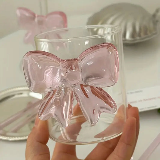 Clear glass with a pink bow decoration held by a hand on a light background