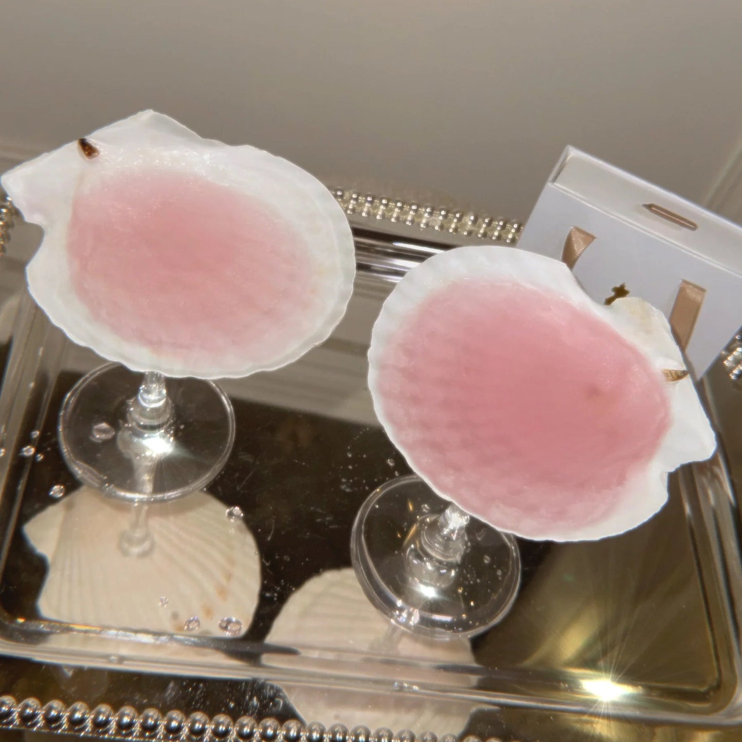 Two shell cocktail glasses in a clear container with a silver rim.
