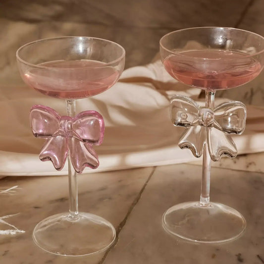 Two cocktail glasses with pink bows on a wooden surface