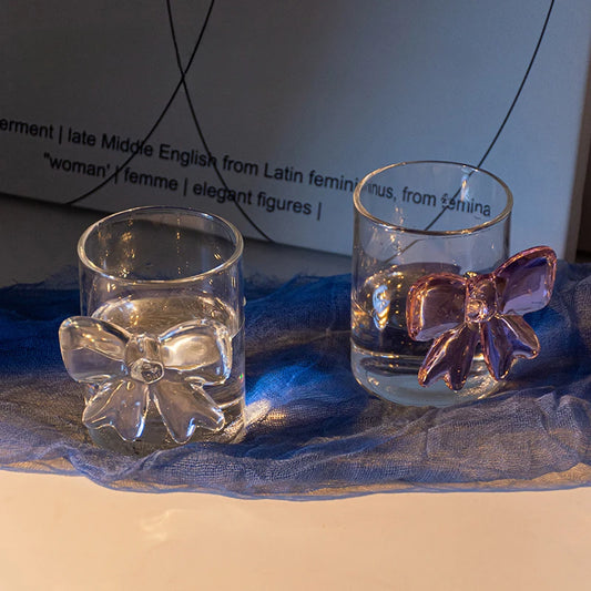 Two clear glass tumblers with bow-shaped decorations on a blue fabric background.
