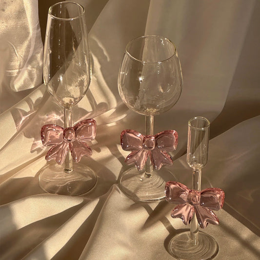Three glass drinkware with pink bow accents on a reflective surface.