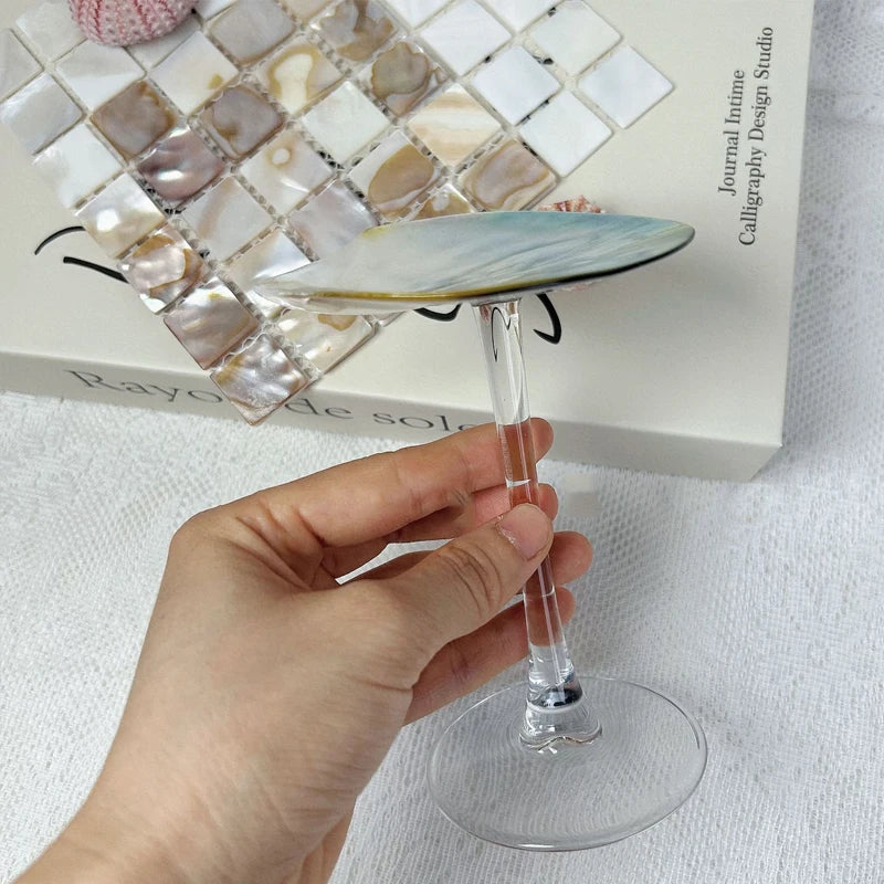 Hand holding a glass with a decorative dish on top, against a white background