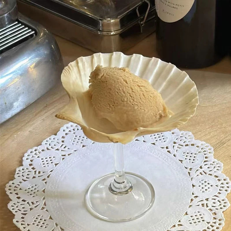 Ice cream scoop in a glass bowl on a doily with a bottle in the background