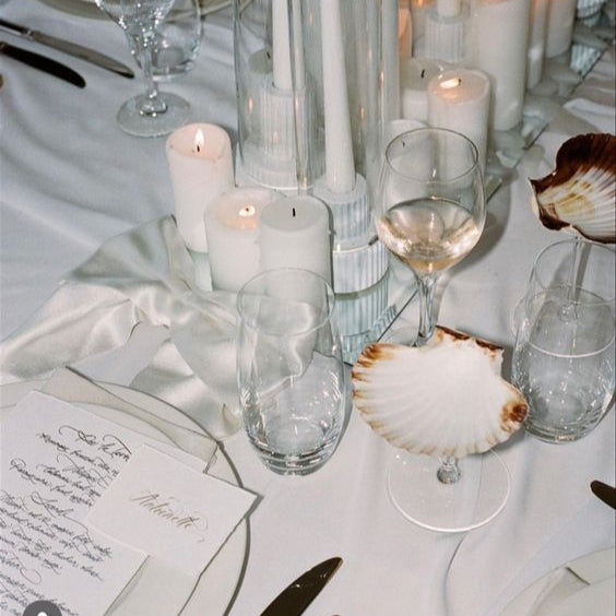Elegant table setting with candles, glasses, and shell decorations on a white tablecloth.