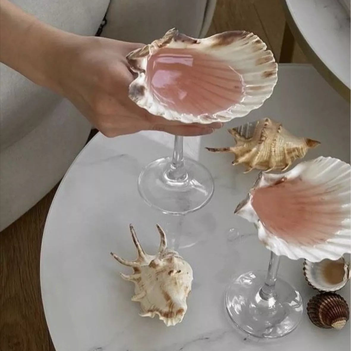 Person holding a shell over a glass with more shells on a marble surface