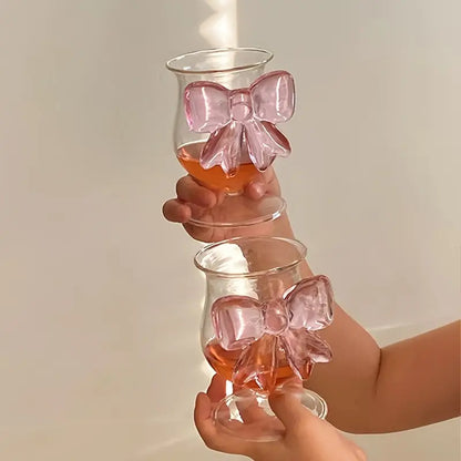 Two glass tumblers with pink bows held by a person against a neutral background