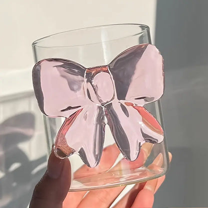 Clear glass with a pink butterfly design held by a hand against a neutral background
