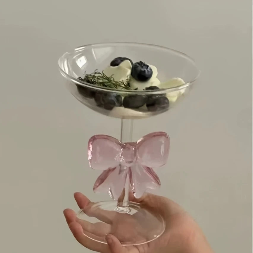 Clear glass with pink bow handle held by a hand against a plain background