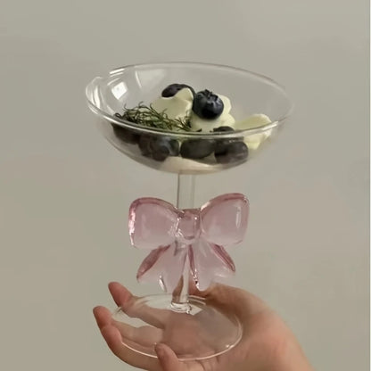 Clear glass with pink bow handle held by a hand against a plain background