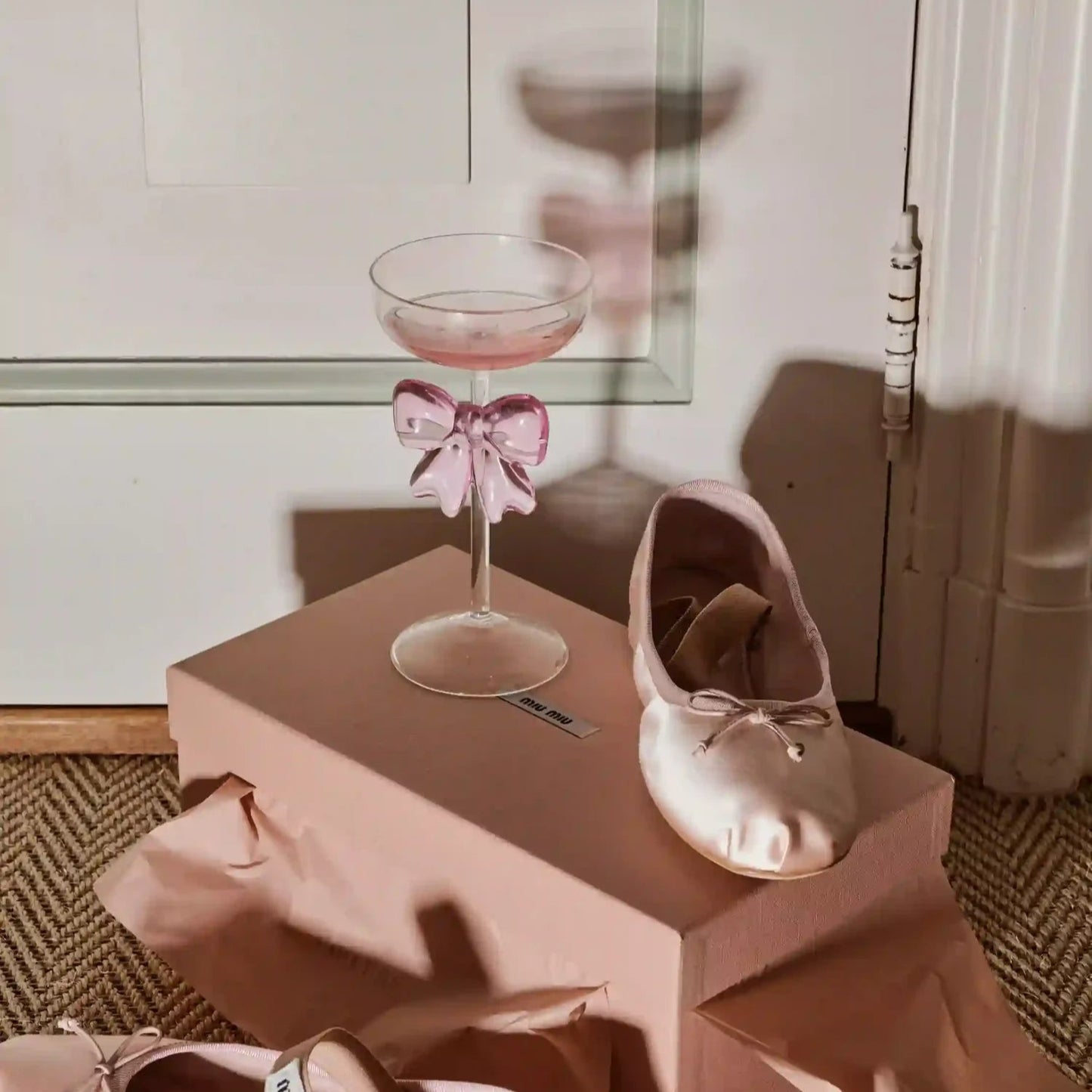 Pink ballet shoes on a small table with a glass holder featuring a pink bow.