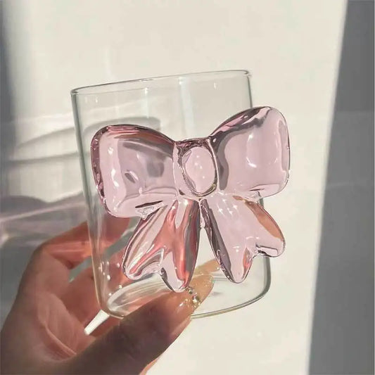 Clear glass with a pink bow design held by a hand on a light background