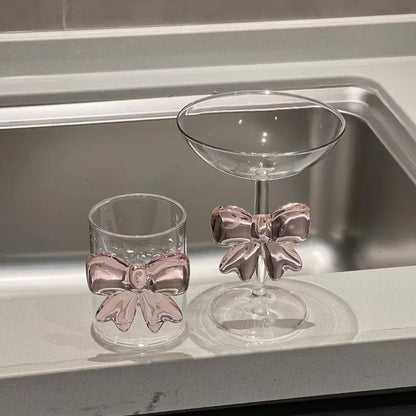 Two glass drinkware items with bow designs on a metallic surface.