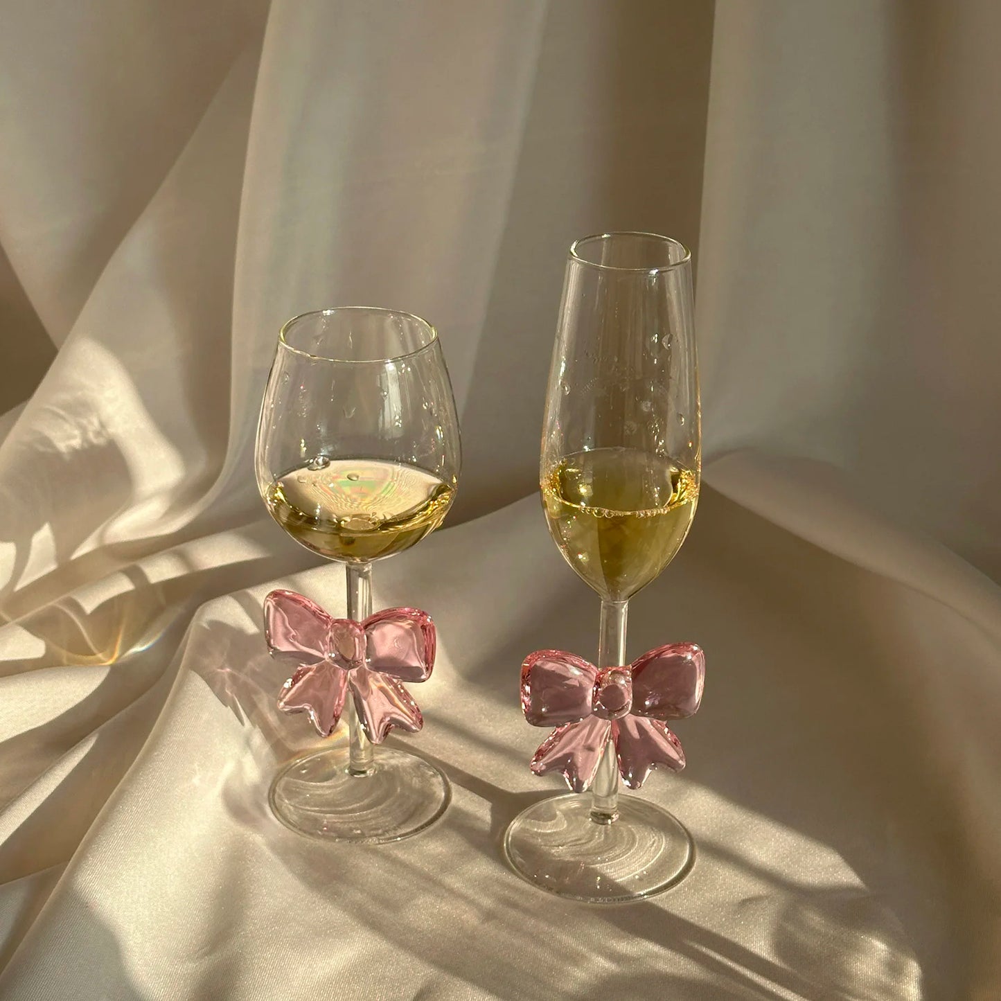Two glasses with pink bows on a light fabric background
