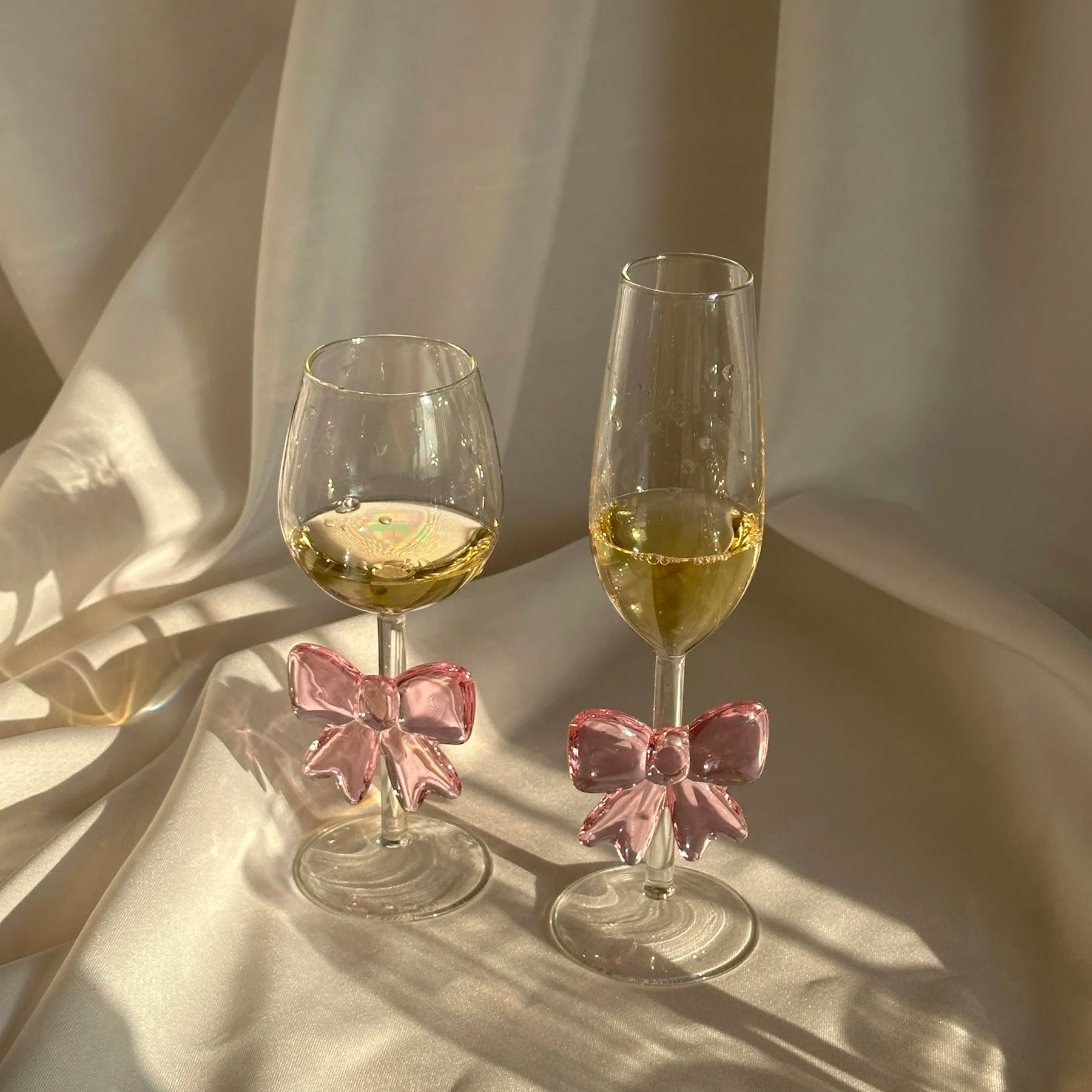 Two glasses with pink bows on a light fabric background