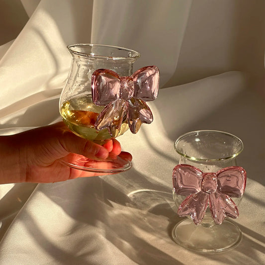 Two glass candle holders with pink bow decorations on a light fabric background.