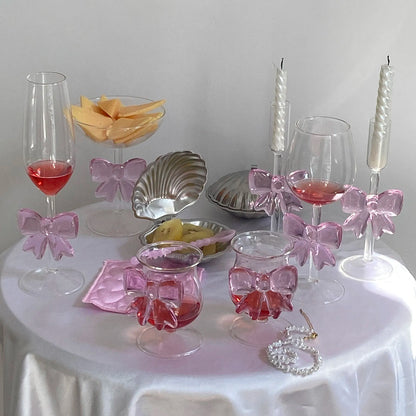 Decorative table setting with glasses, bowls, and pink bows on a white surface.