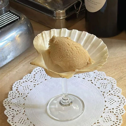 Ice cream scoop in a glass bowl on a doily with a bottle in the background