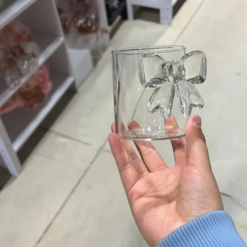 Clear glass mug with a handle held by a hand on a light-colored floor.