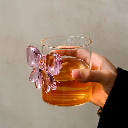 Hand holding a glass with a pink bow handle against a neutral background